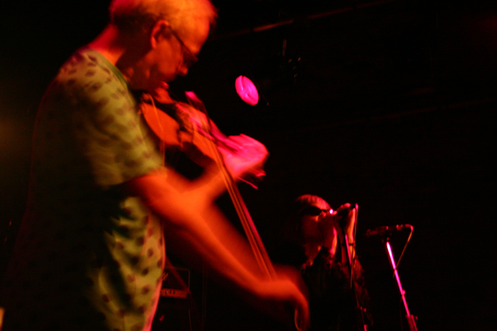 Tony conrad bowing a violin in the foreground, Keiji Haino singing behind