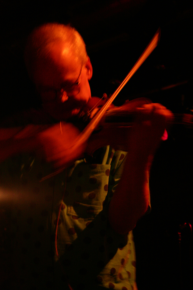 Close up of Tony Conrad bowing a violin wearing a green shirt