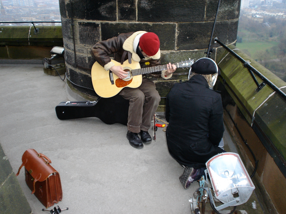 a guitarist and singer perform at the top of the Glasgow University Bell Tower