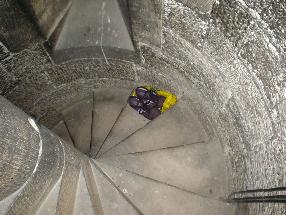 A view looking down a stone spiral staircase. A pair of trainers is on a step.