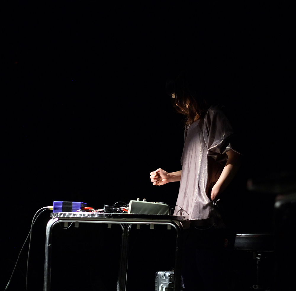 Sachiko M in a purple shirt stands at table as she plays a mixer