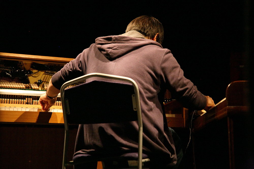 Otomo Yoshihide sits back to the camera playing two upright pianos