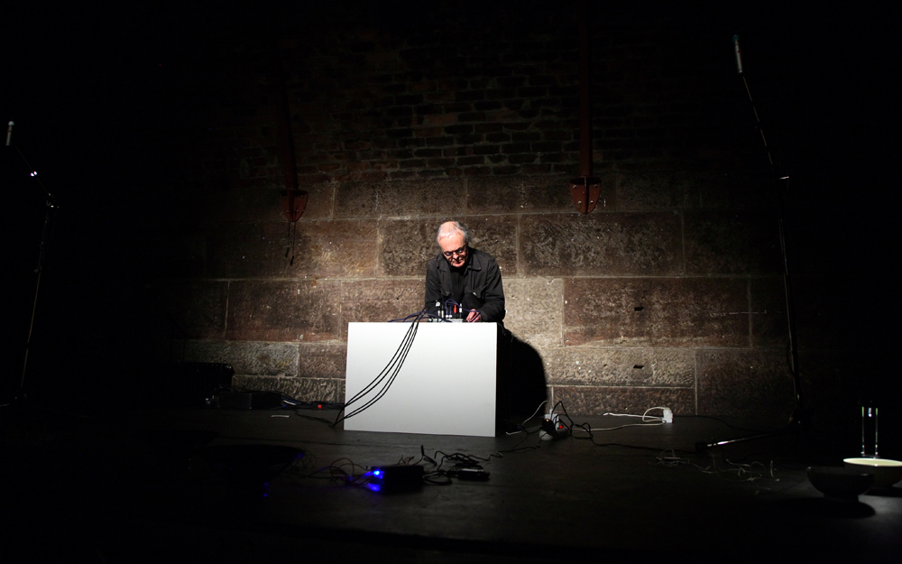 Rolf Julius leans forward over a large white box and mixer and performs