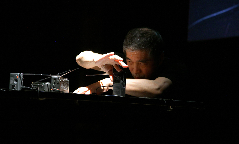 Tetsuo Kogawa peers at several small radios as he manipulates the aerial of one