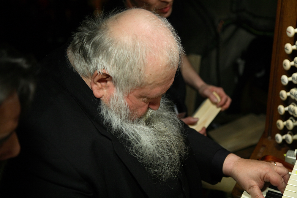 A bald and beared Hermann Nitsch looks down as he plays the organ