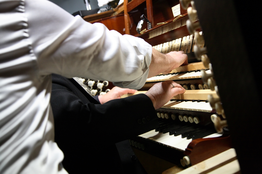 A tangle of shirted arms and arms play at an organ keyboard