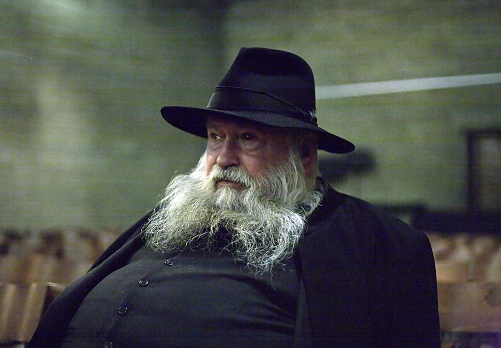 Herman Nitsch in a large hat and black button jacket with a grey beard