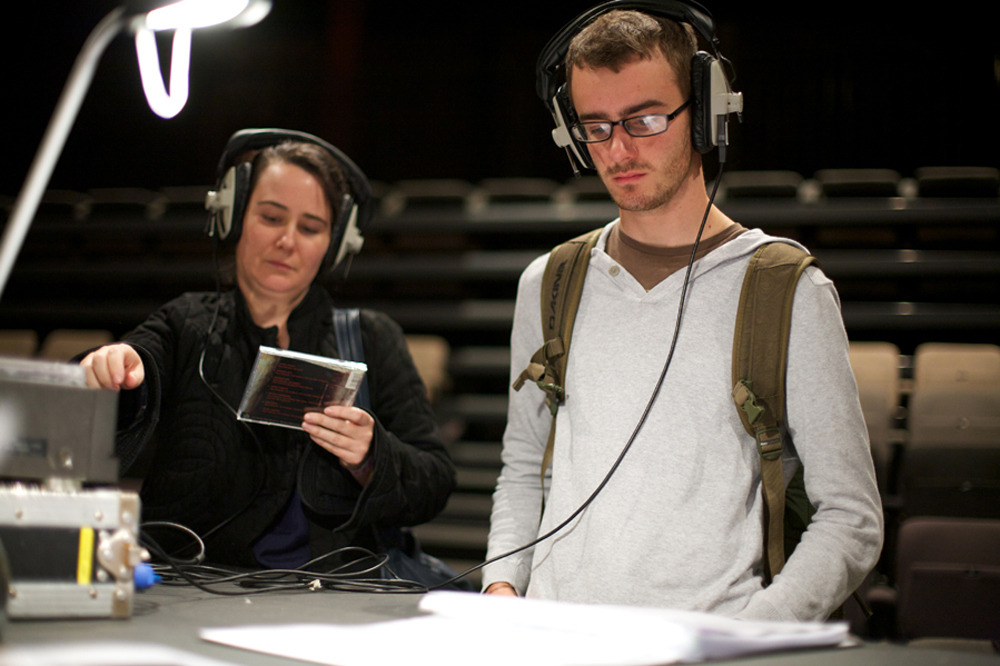 Two people with headphones listen to items in an installation at a large table
