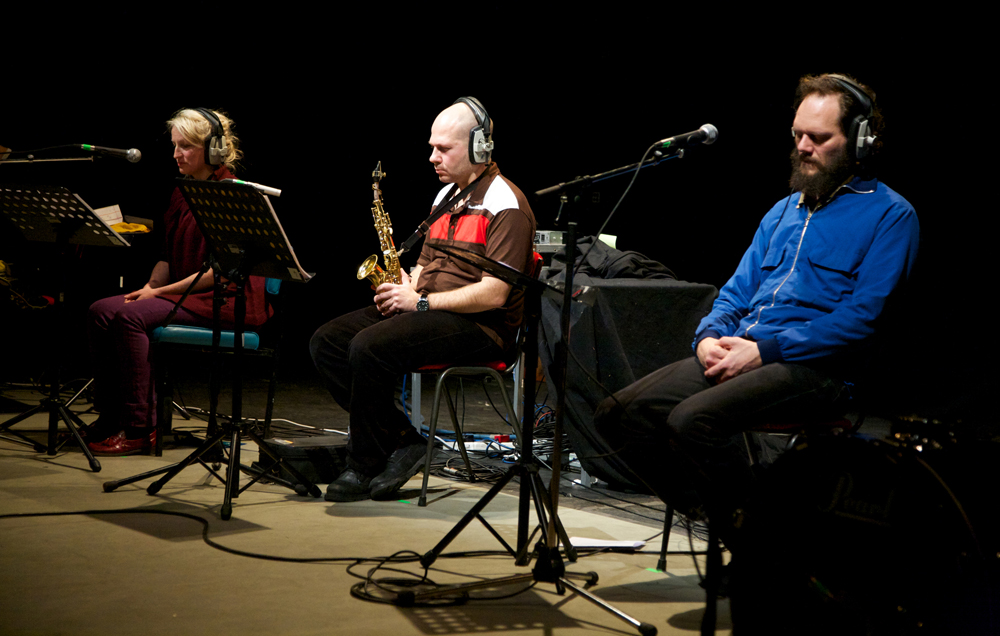 Three sitting performers with headphones 