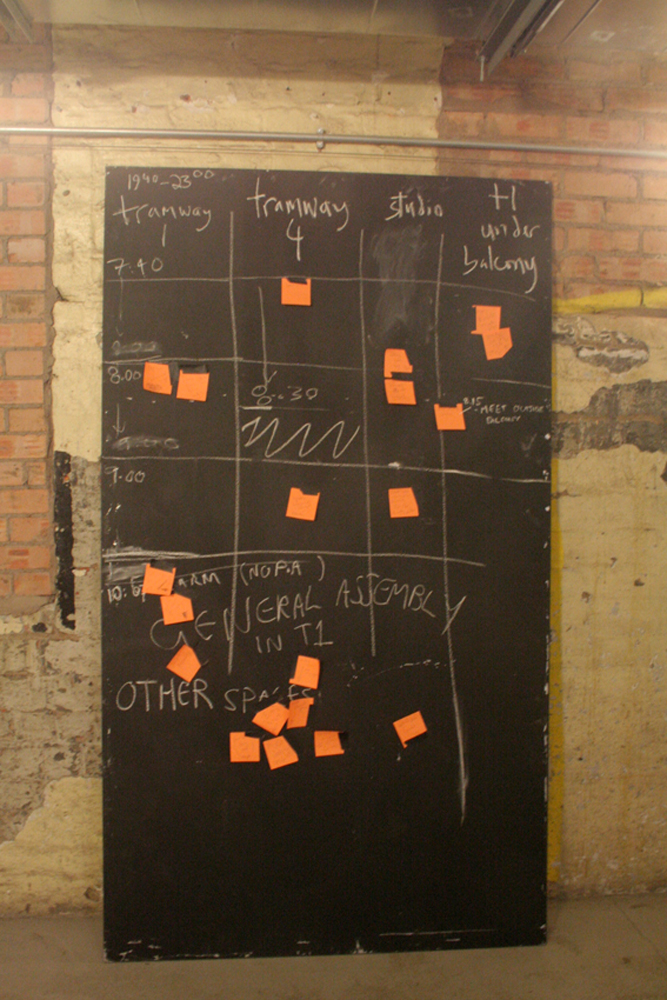 A blackboard with chalk lined box shapes and orange post-it notes by a wall