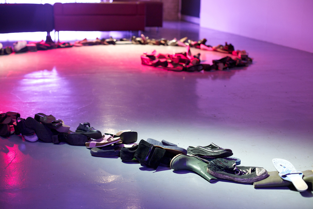 A spiral form made of shoes and boots is laid out on a purple and red lit floor