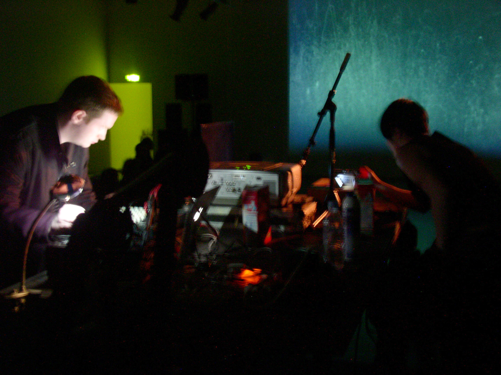 Two people operating equipment against a projection screen