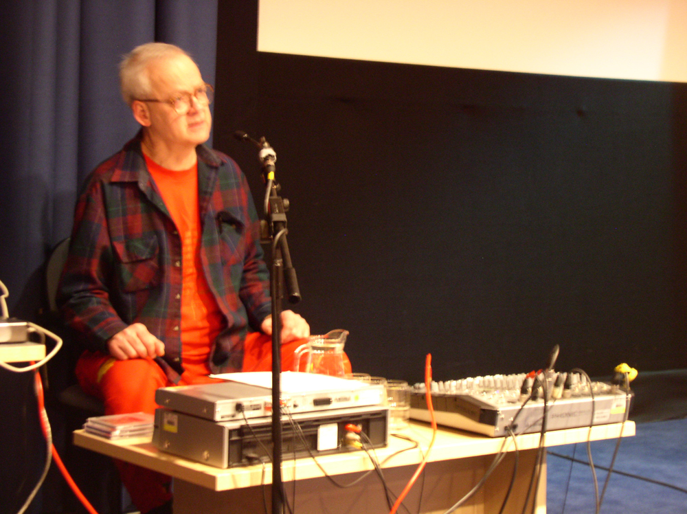 Tony Conrad wearing a shirt and orange t shirt looks forlorn