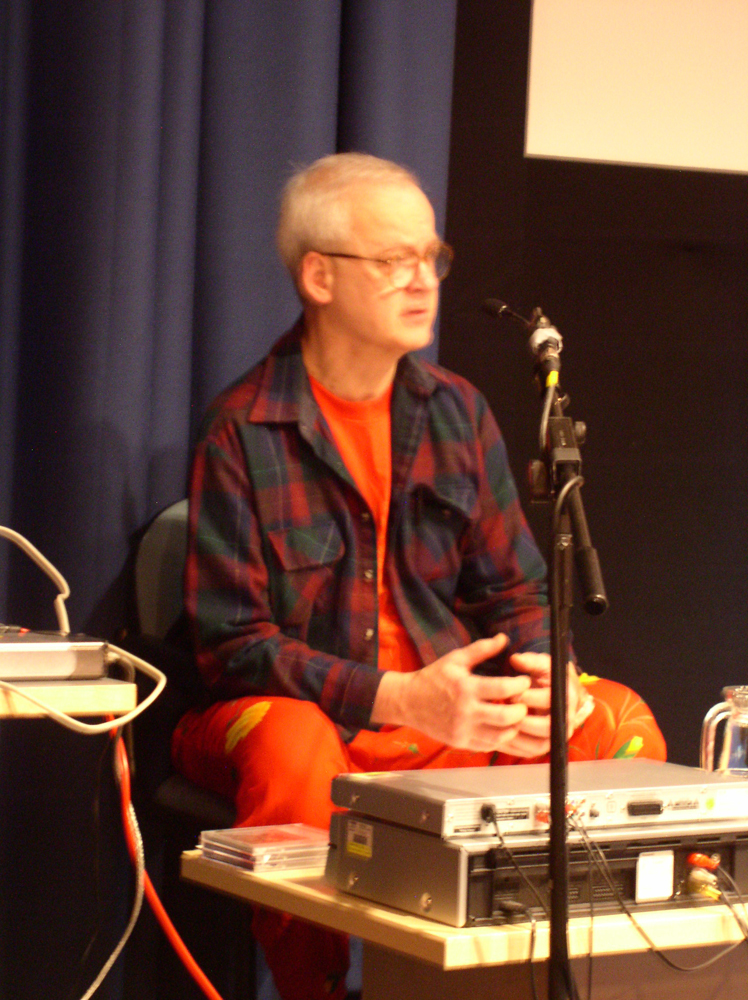 Tony Conrad seated in orange tropical fruit patterned trousers