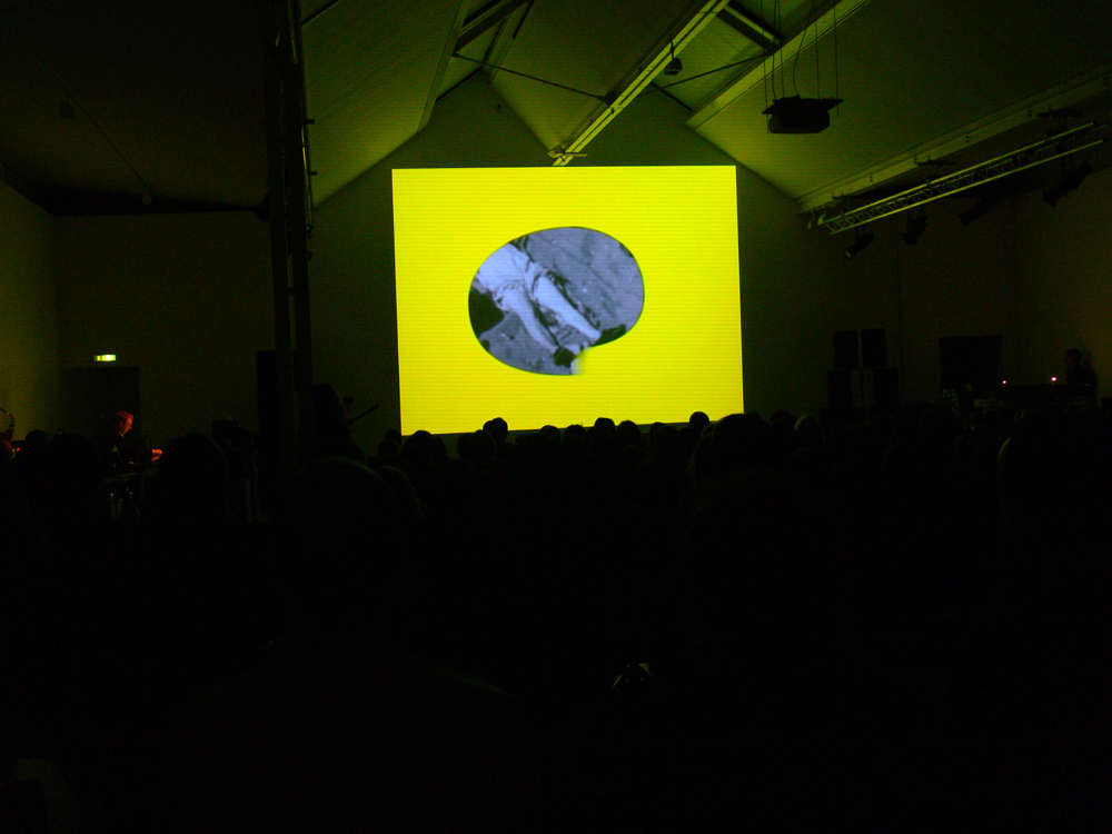 A person's legs framed in lemon yellow on a screen before an audience