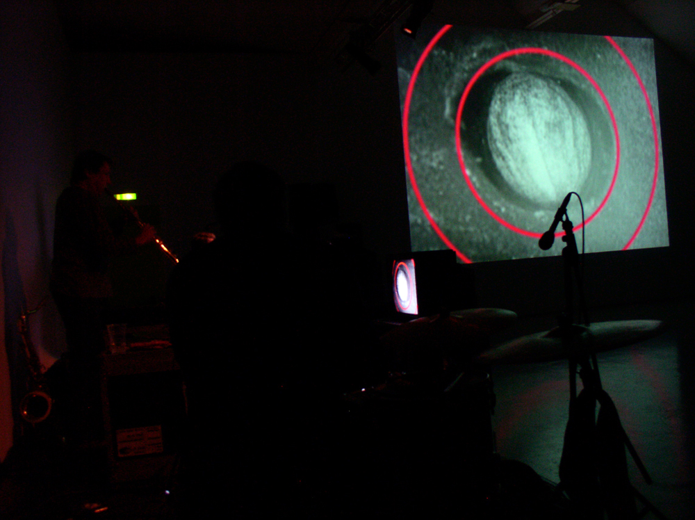 Screen showing an orb circled in pink rings near some musicians in the dark