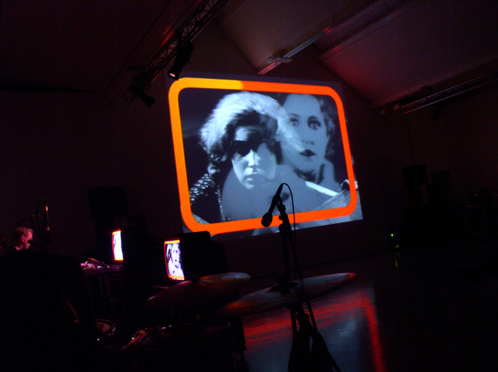 Two women's faces on a screen with orange frame added, reflections on the floor