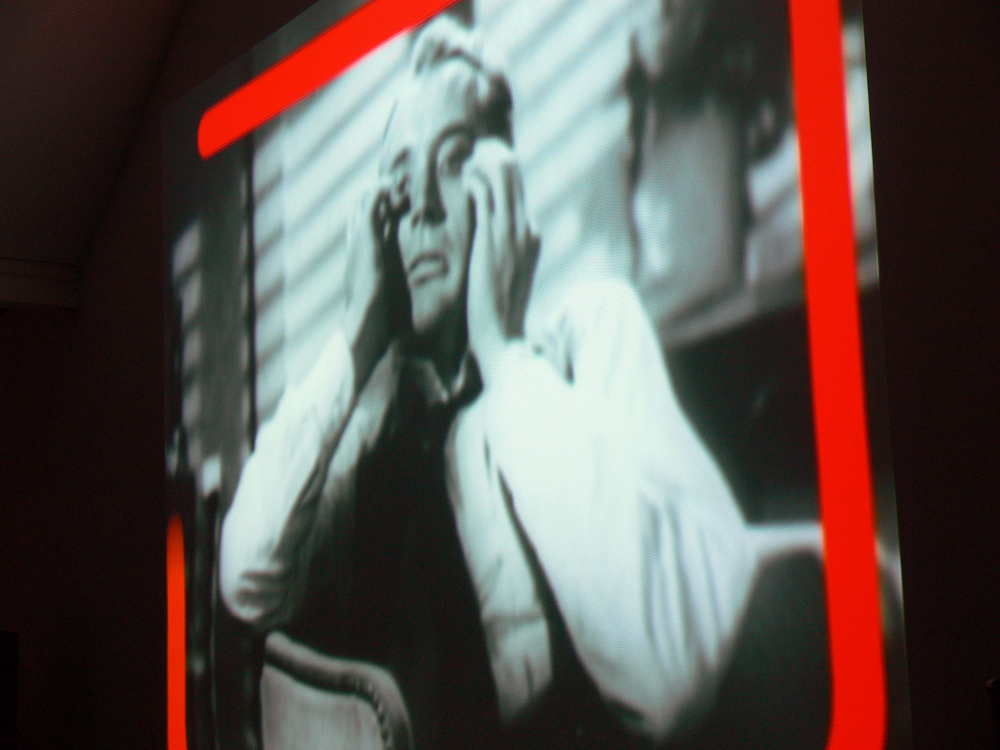 A projection of a man holding his hands up to his face as a red line borders 