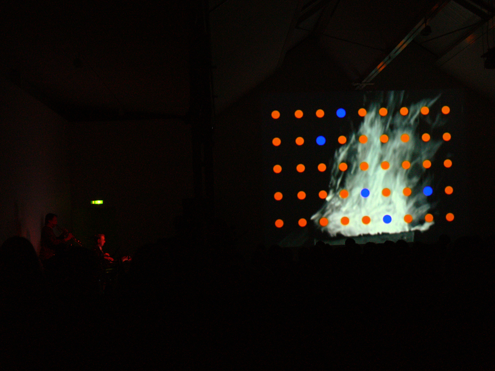 Musicians on the left in the dark, right is a screen with orange dots in a grid