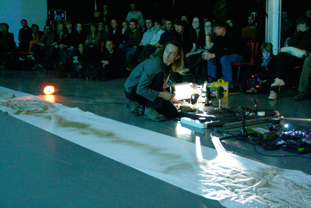 A man crouching before an audience operating a projector