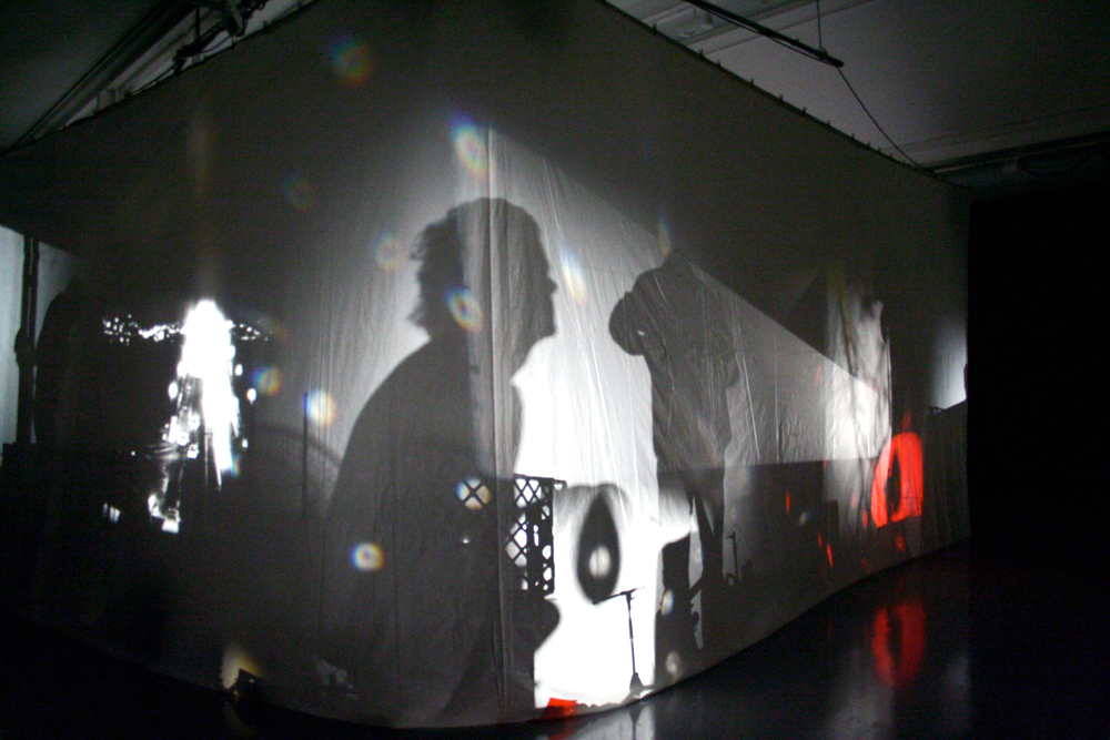 Some figures and equipment casting shadows on a fabric screen