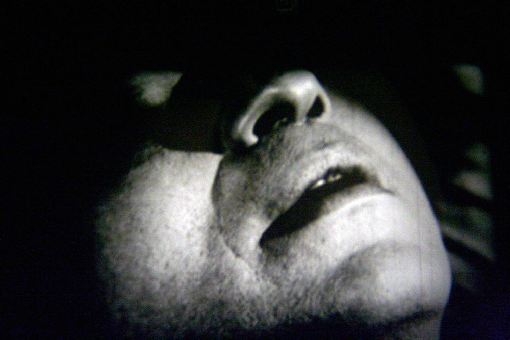 The jaw, mouth and nose of a man's face, the rest in shadow