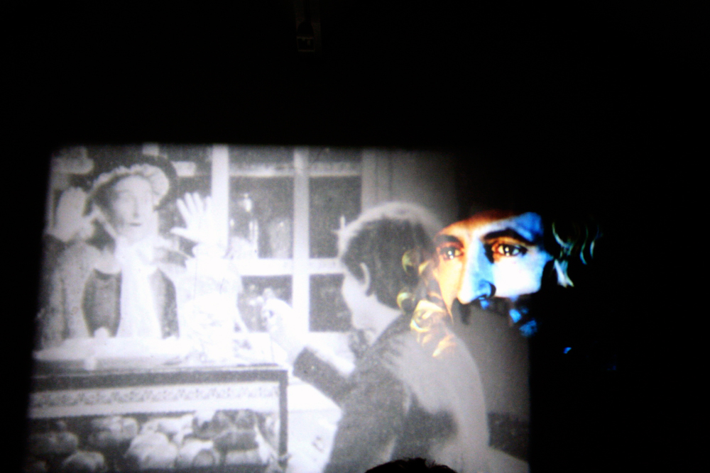 Black and white projections with a wigged man appearing in colour on the right
