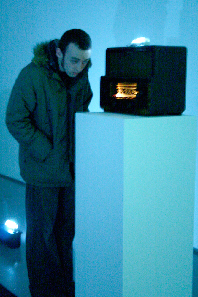 A man inspects a radio on top of a plinth in blue light