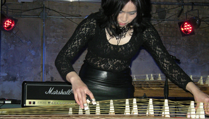 Michiyo Yagi in a black lace top bends to pick the strings of the Koto