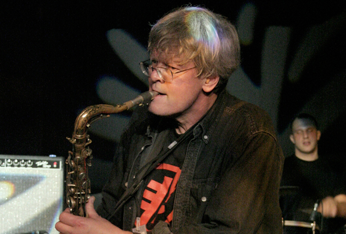 Don Dietrich with shaggy grey hair puts his saxophone to his mouth
