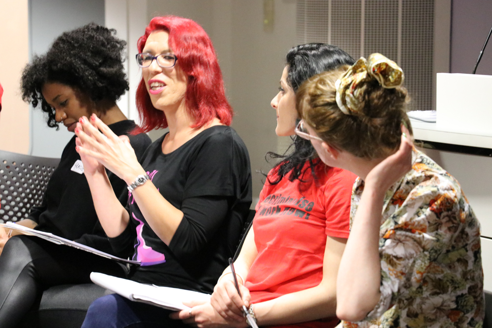 Four People sitting in a row, one in red hair talking