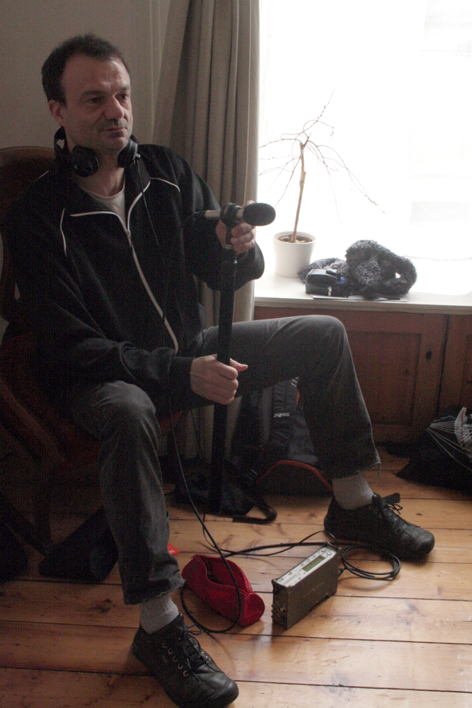 Jean-Luc Guionnet sitting in a home with a microphone and recording gear 