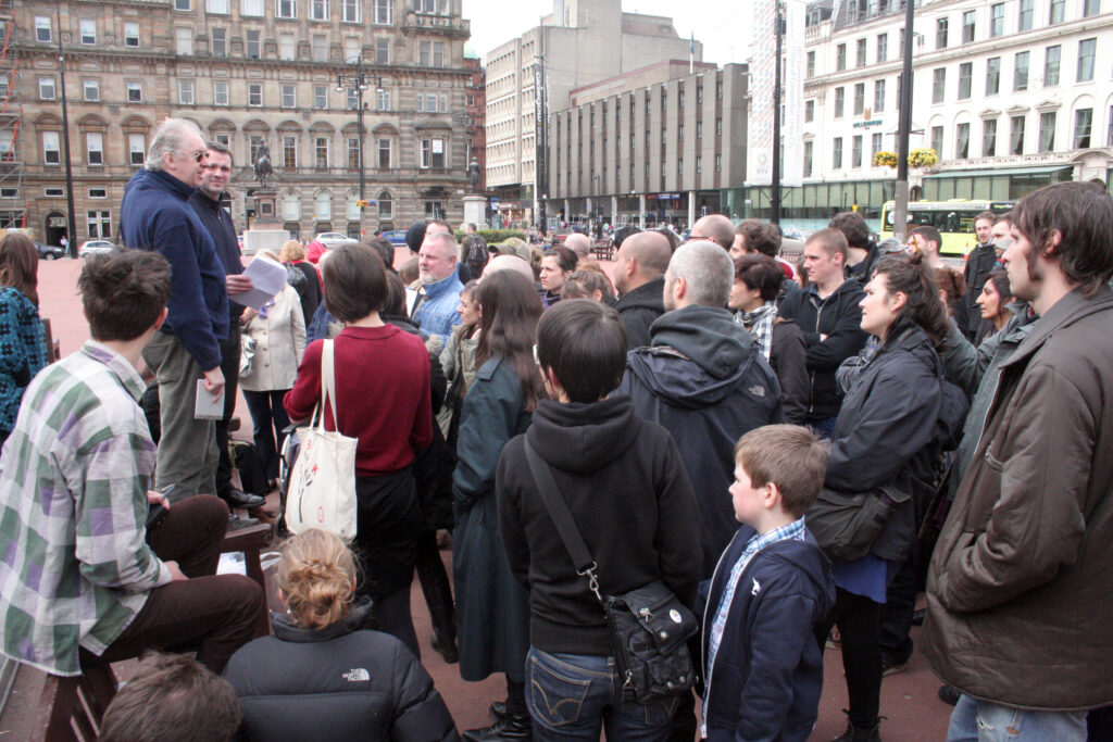 A group of people huddle round a speaker in George Square, Glasgow