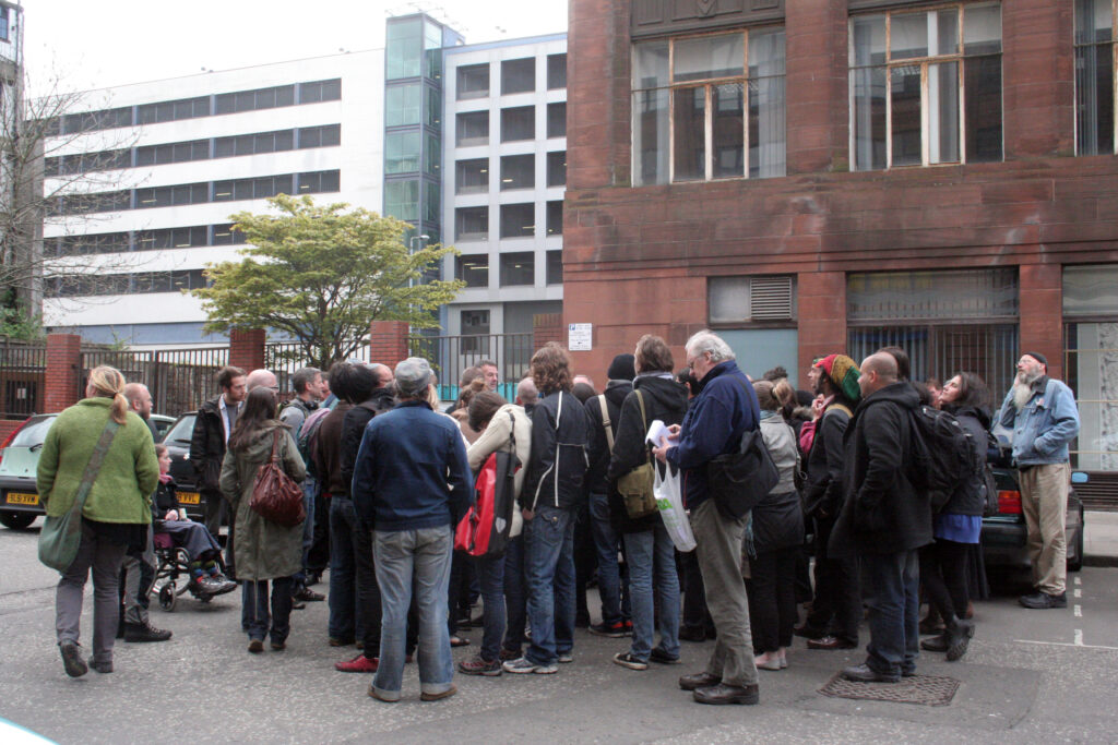 People huddled around a speaker on a street in Glasgow