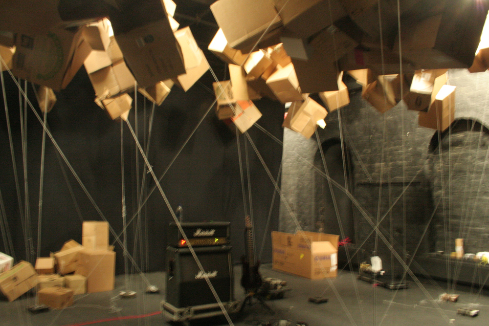 Guitar amplifier amidst cords suspending cardboard boxes