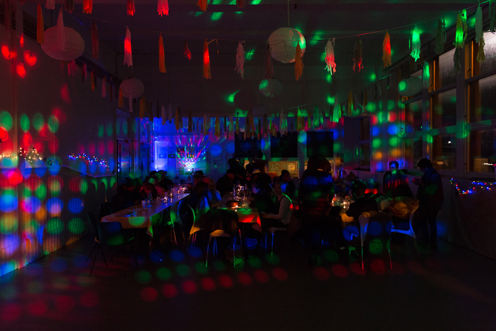 A room is covered with disco lights as people gather at tables