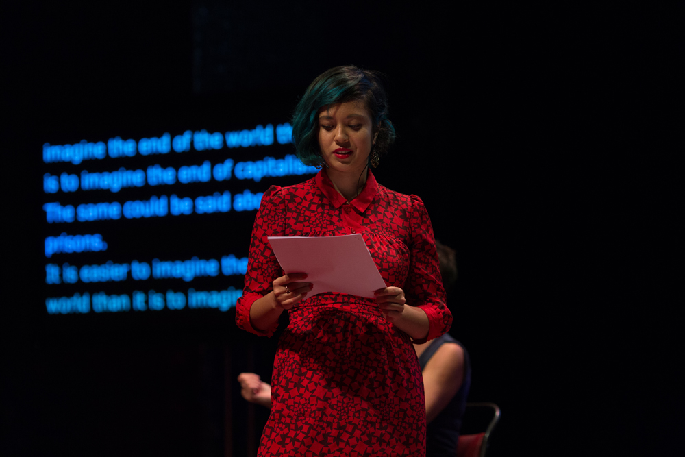 Jackie Wang reading in a red dress on stage in front of a transcription screen