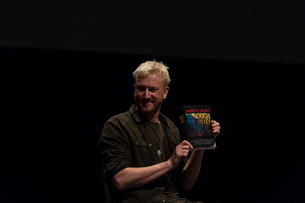 Barry Esson with quizical expression holding up a copy of a Samuel Delany book