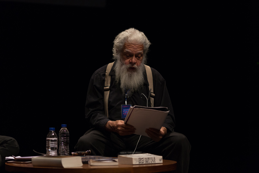 Samuel Delany reading from a document on stage; bearded with grey hair & braces