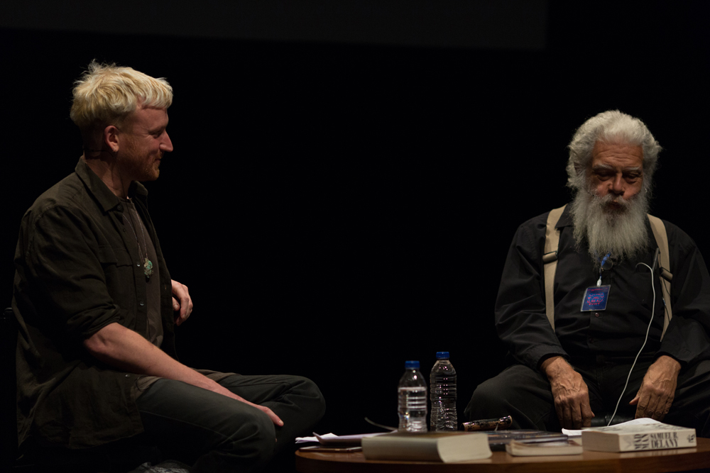 Barry Esson and Samuel Delany in black talking on stage next to a table