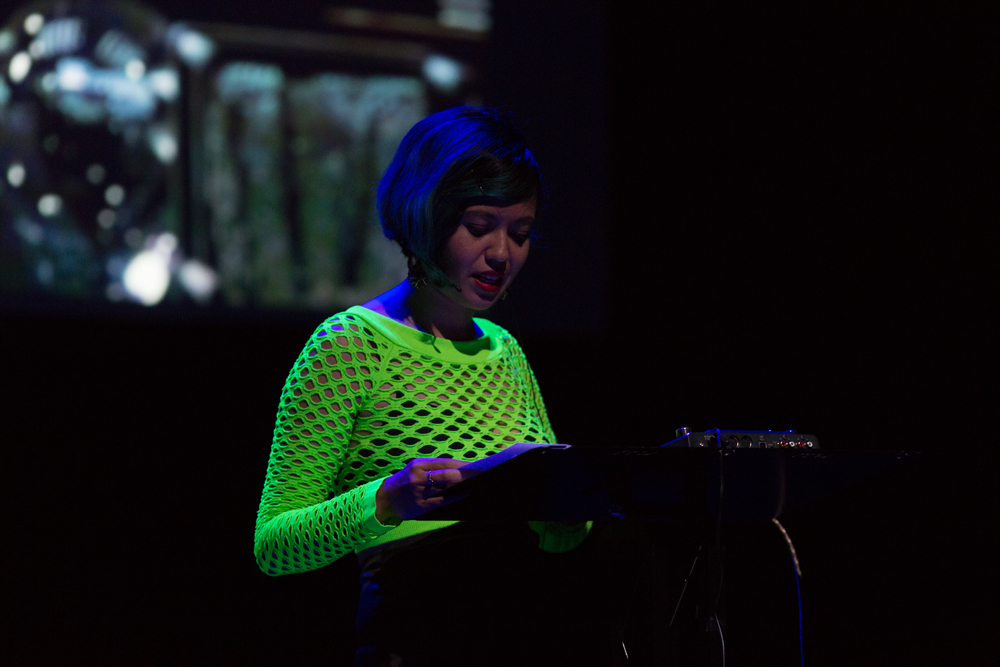 Jackie Wang reading from a lectern in front of a projected metallic surface