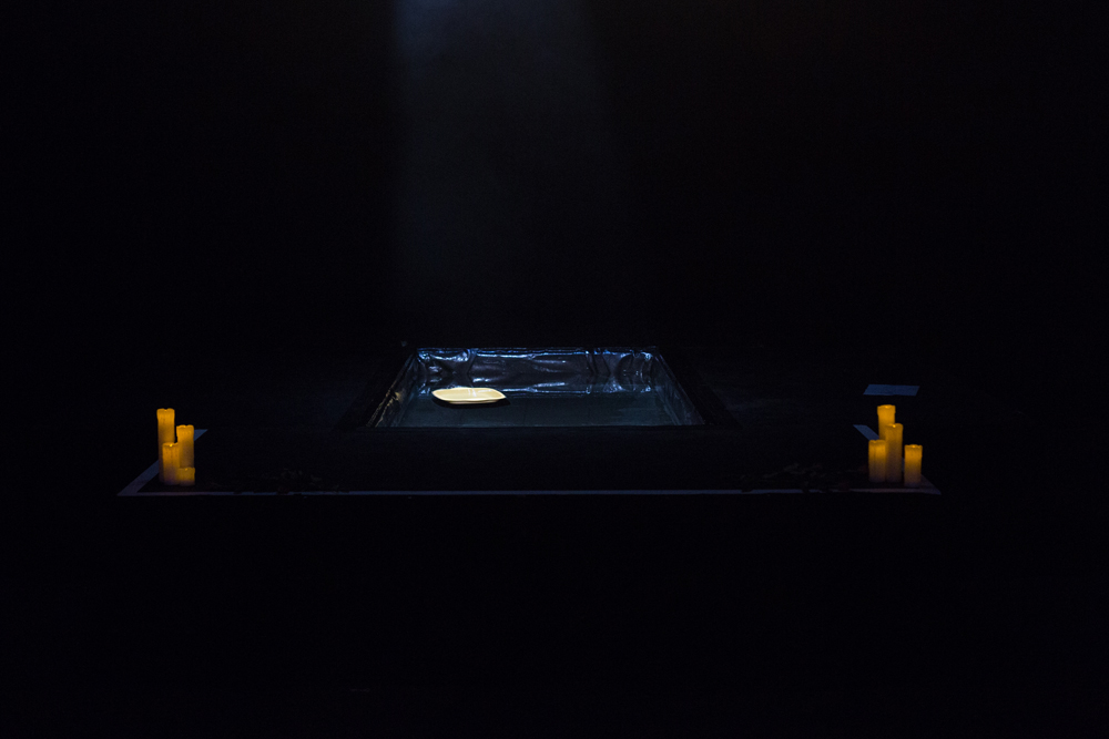 Yellow candles and a recessed pool of water on stage in dim lighting