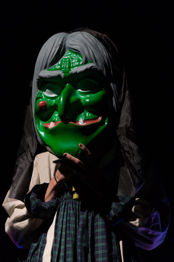 A huge green witch mask obscures a performer's features