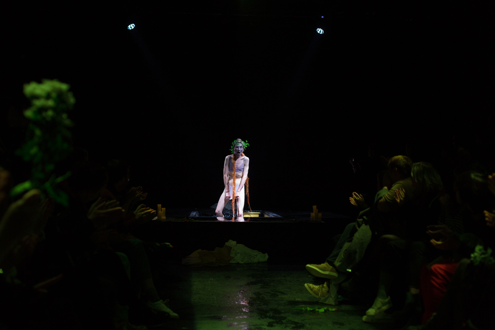 A pastoral figure adjusting her pants in a pool of water surrounded by audience