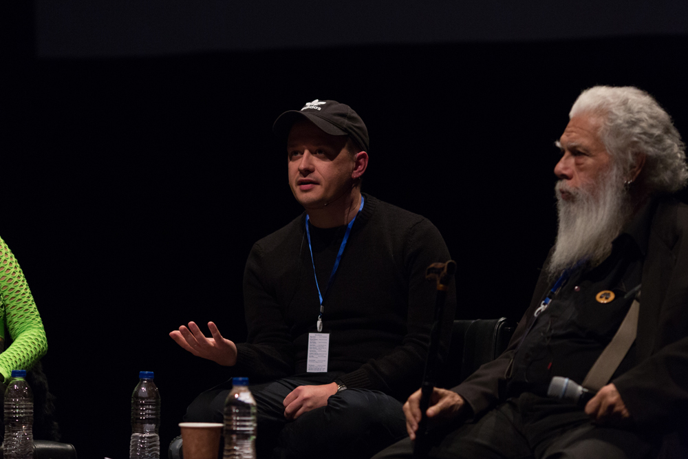 Huw Lemmey wearing a cap talking while Samuel Delany listens