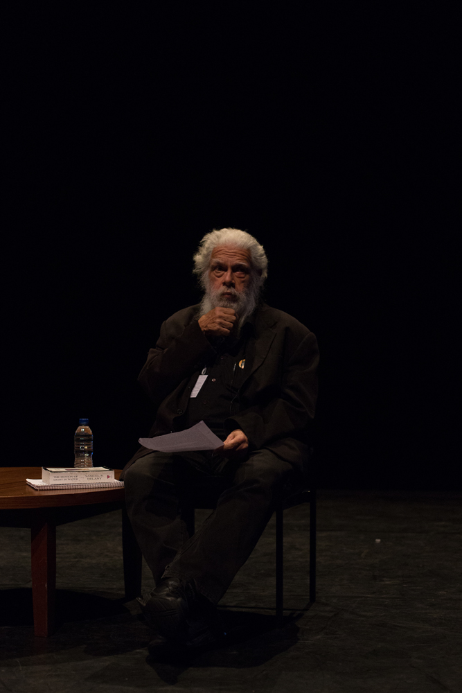Samuel Delany holding his fist to his chin seated next to a table with papers