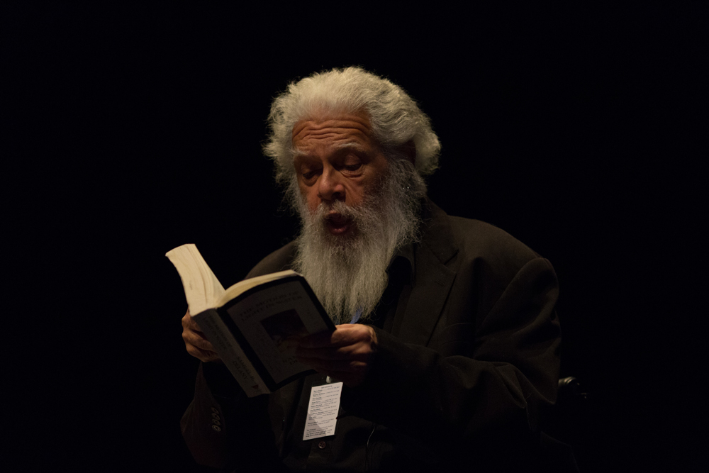 Samuel Delany wearing black and bearded reads from a book 