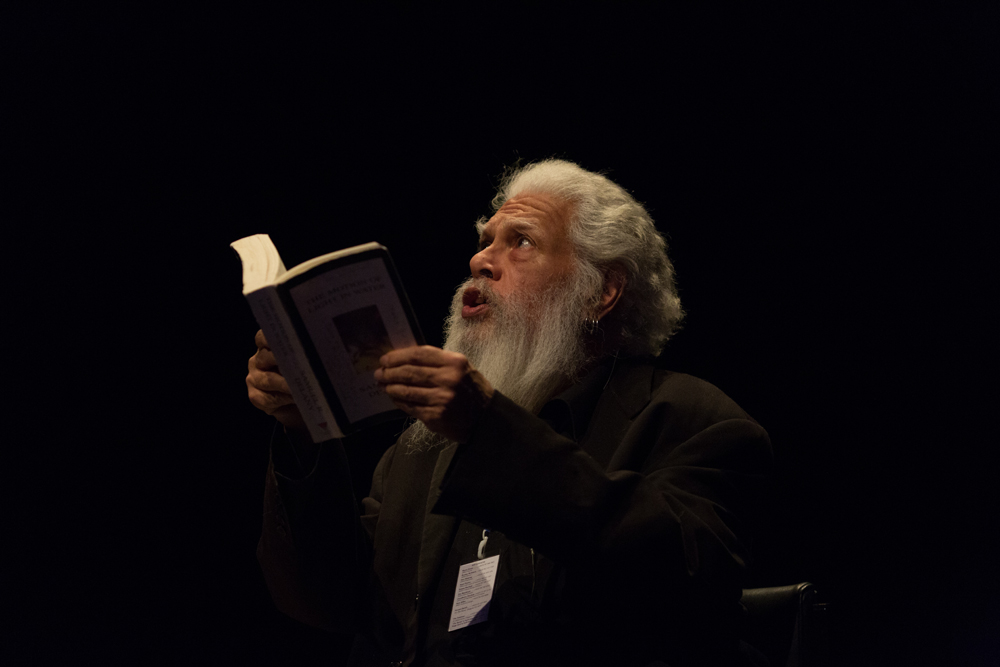 Samuel R. Delany white hair and beard reading on stage at EPISODE 9