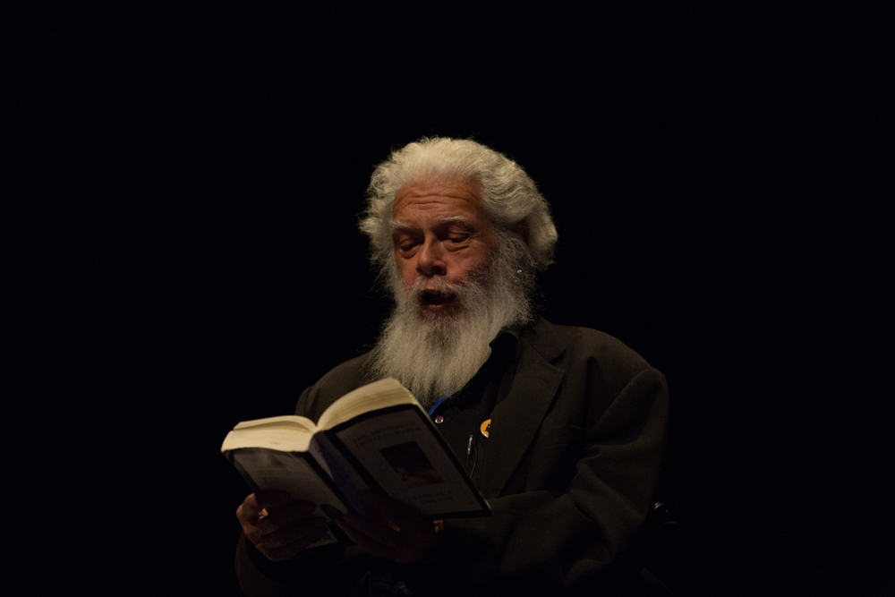 Samuel Delany wearing black and bearded reading from a book 