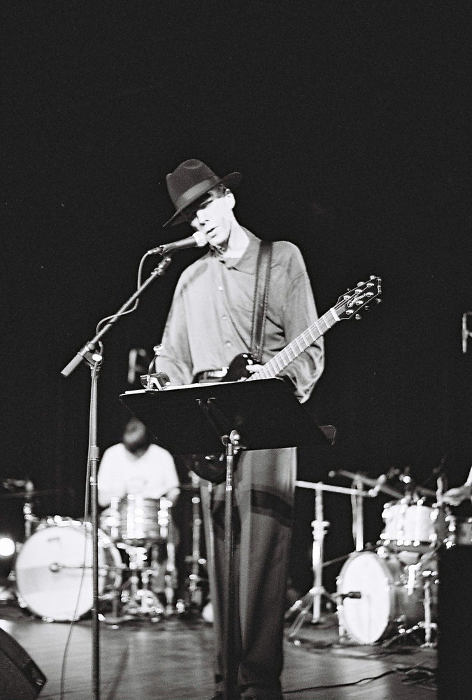 Jandek with two drummers on stage in Austin
